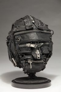 Ronald Gonzalez -  <strong>Zipped (side)</strong> (2018<strong style = 'color:#635a27'></strong>)<bR /> black leather, found objects, wire, wax, carbon, screws and metal filings over welded steel armatures,
11 x 9 x 9 inches